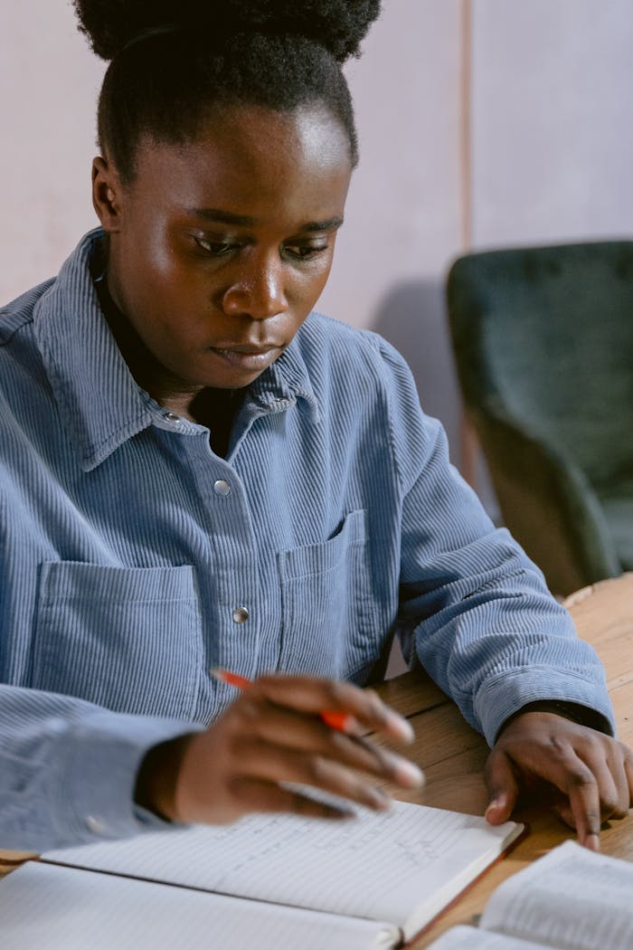 Young woman intensely writing in a notebook while seated at a desk, deep in thought.